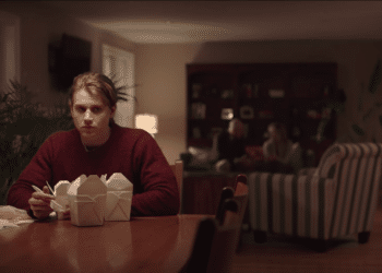 Jason Hodges (Alex Saxon) sitting on a table with some food in the Netflix movie 'Coin Heist'.