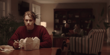 Jason Hodges (Alex Saxon) sitting on a table with some food in the Netflix movie 'Coin Heist'.