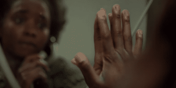 A couple's hands try to touch each other but are separated by prison glass in the movie 'If Beale Street Could Talk'.
