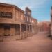 Empty dirt street in an old western town with various wooden buildings. 3D rendering.